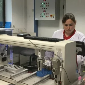 A person in a lab coat operates automated laboratory equipment in a modern laboratory setting.