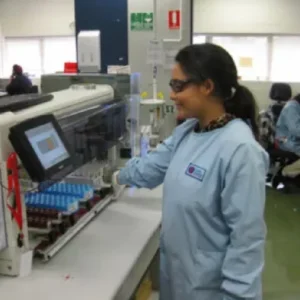 A person in a lab coat and safety glasses operates laboratory equipment with test tubes in a laboratory setting.