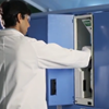A person in a lab coat and goggles operates a PathFinder 900 Plus scientific instrument inside a blue cabinet in a laboratory setting.